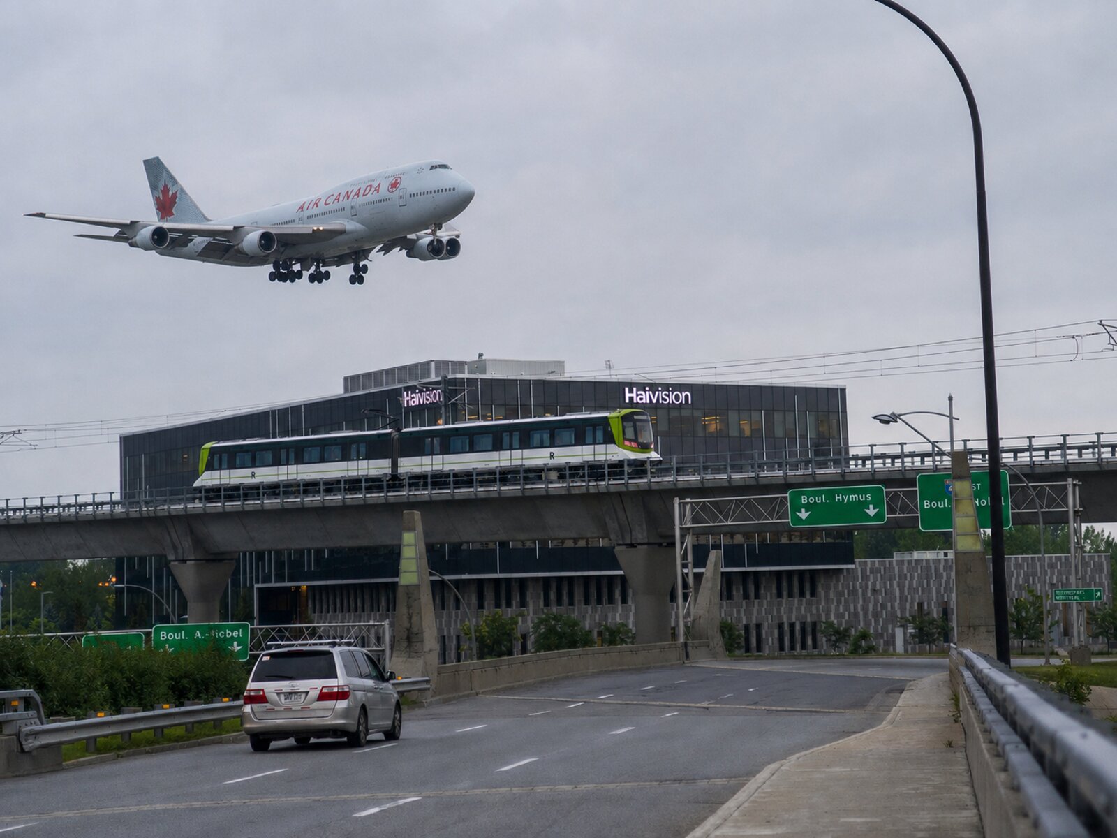 An Air Canada jet on final approach passes over a REM light-rail train on the elevated guideway near Montreal-Trudeau airport